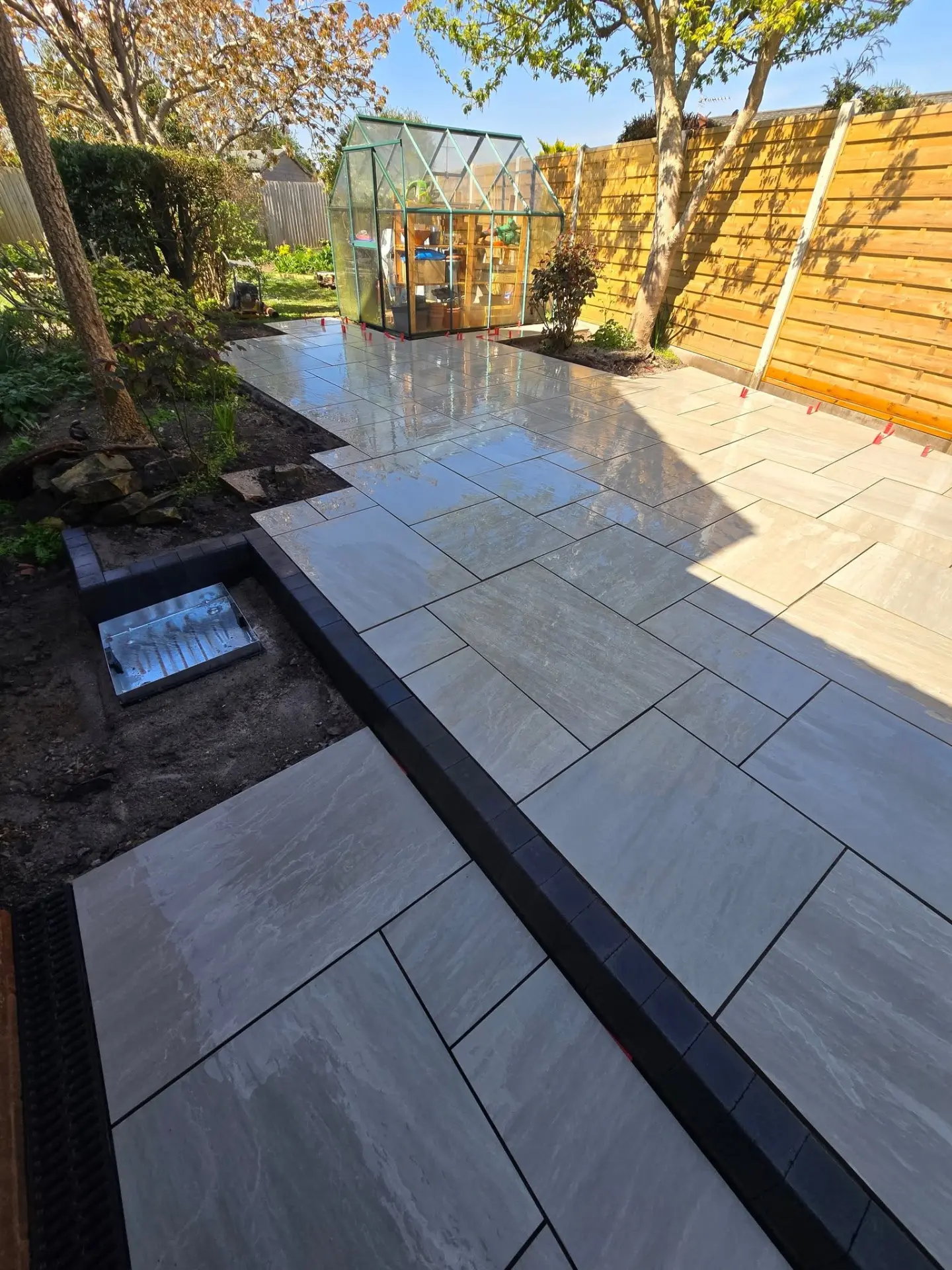 Large light-grey porcelain patio slabs laid beside a garden greenhouse